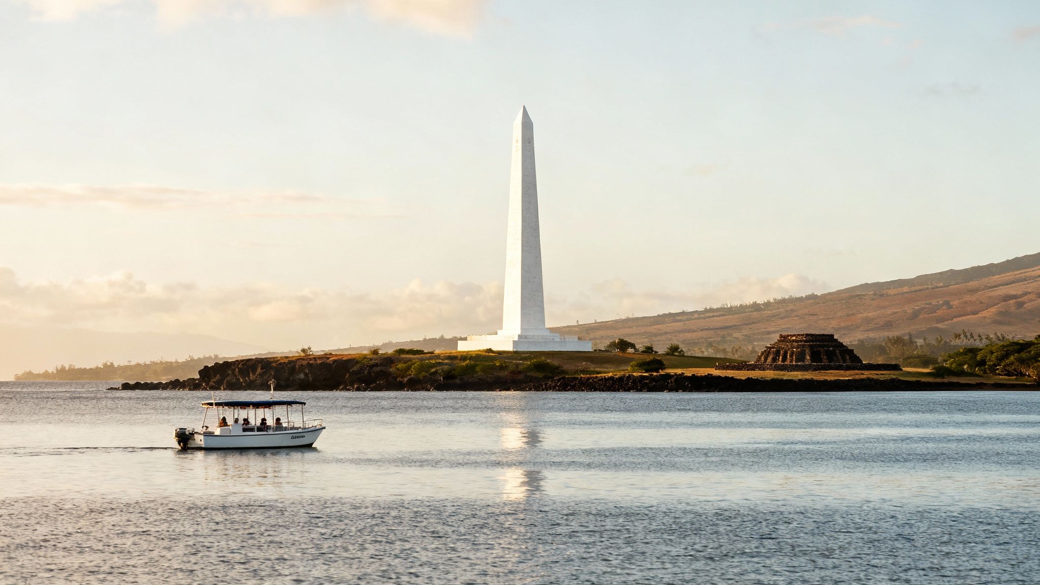 A small tour boat with people cruises past the Captain Cook Monument in Kealakekua Bay, Hawaii.