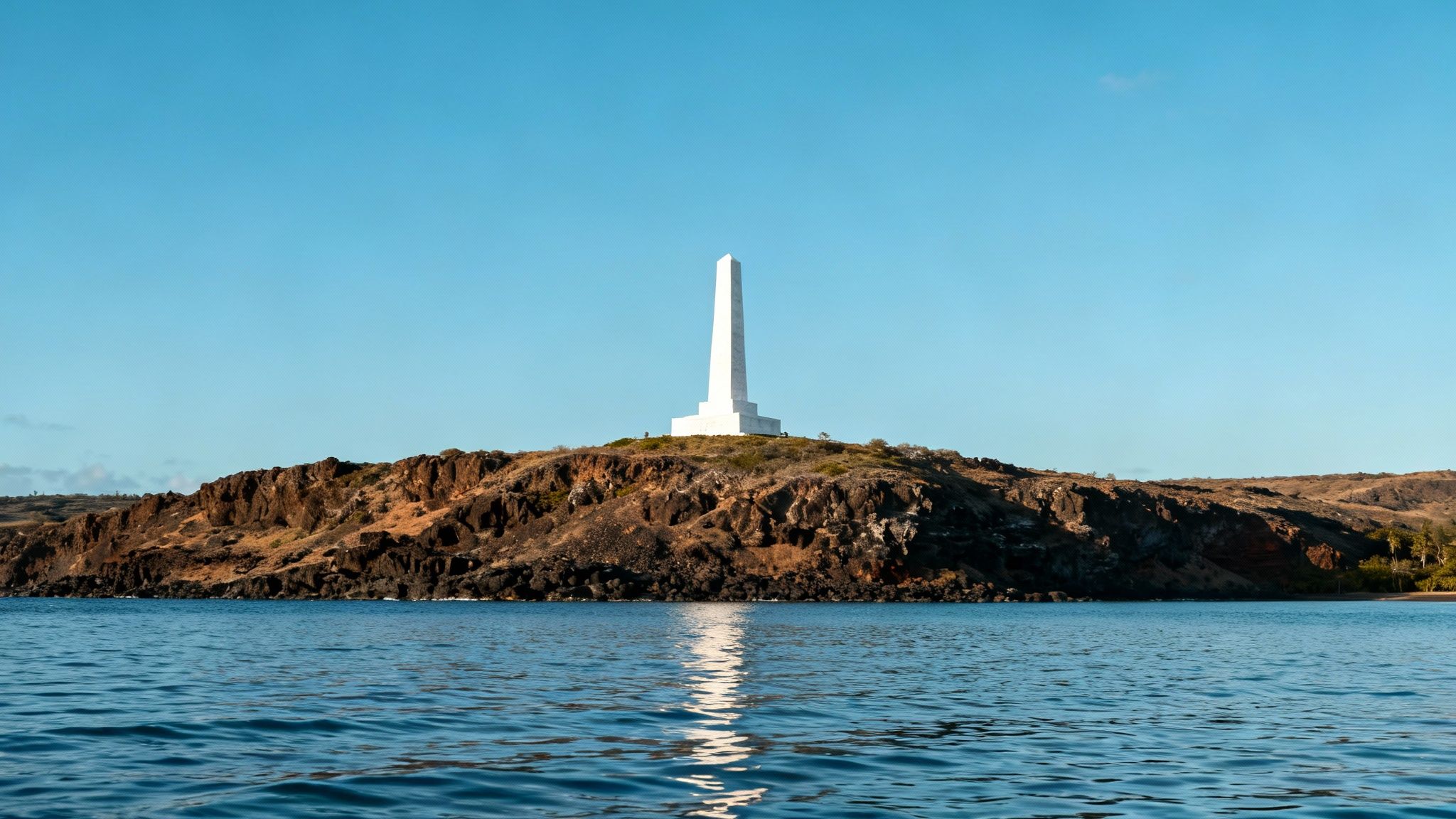 A boat anchored in the stunningly clear turquoise waters of Kealakekua Bay with the Captain Cook Monument in the background.