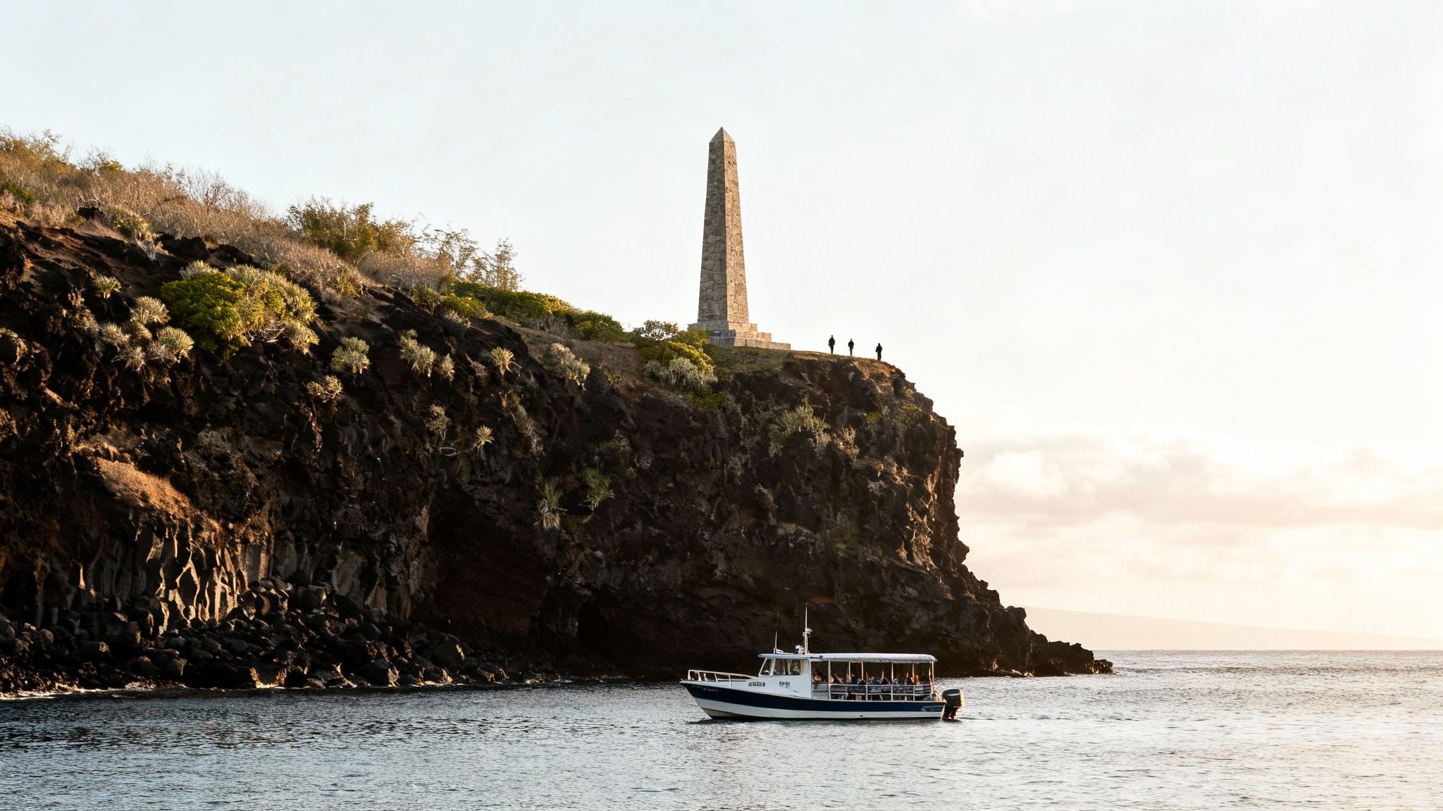 A tour boat with passengers near a rocky cliff with a tall stone obelisk and people on top.