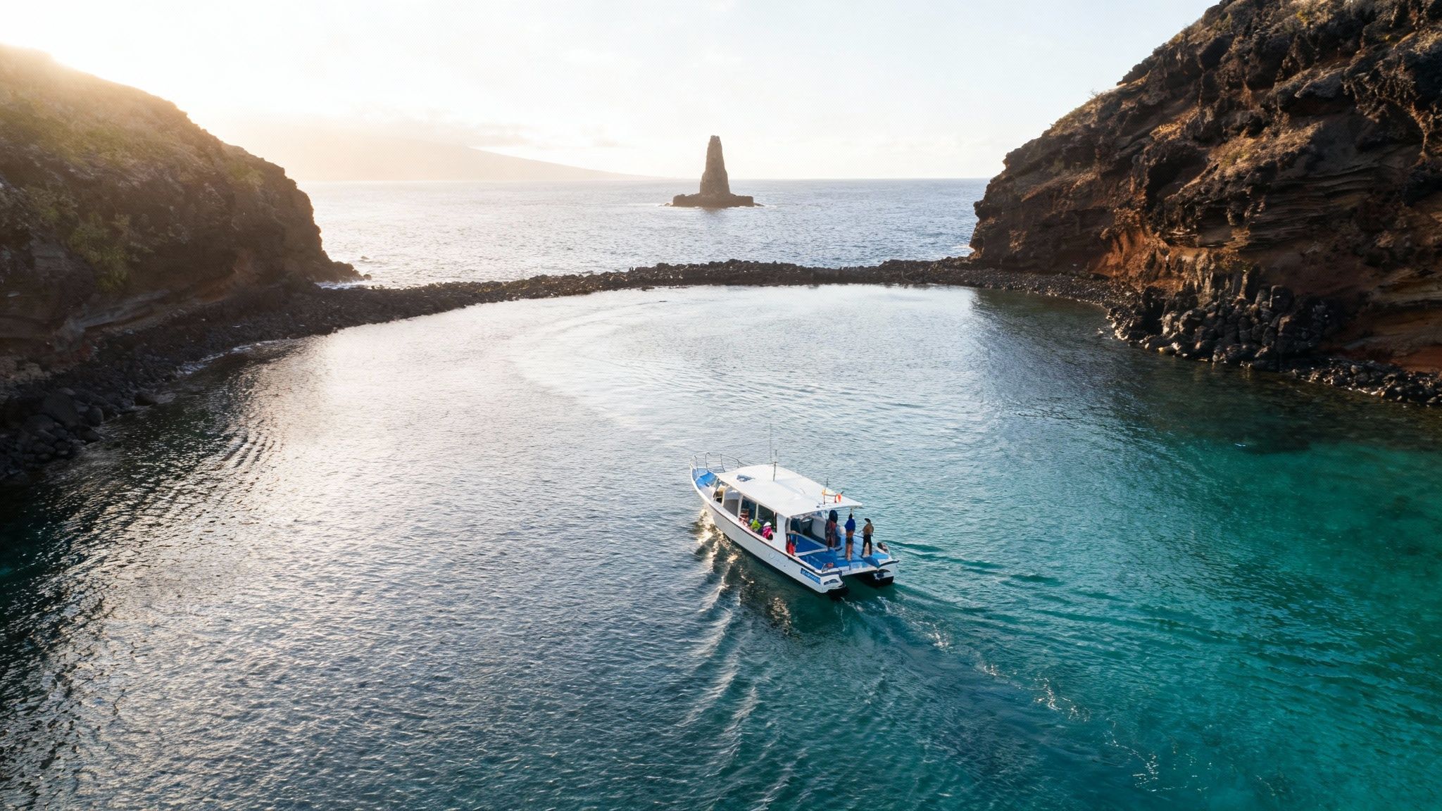 A boat with people in a clear blue bay, surrounded by rocky cliffs and a distant rock formation.