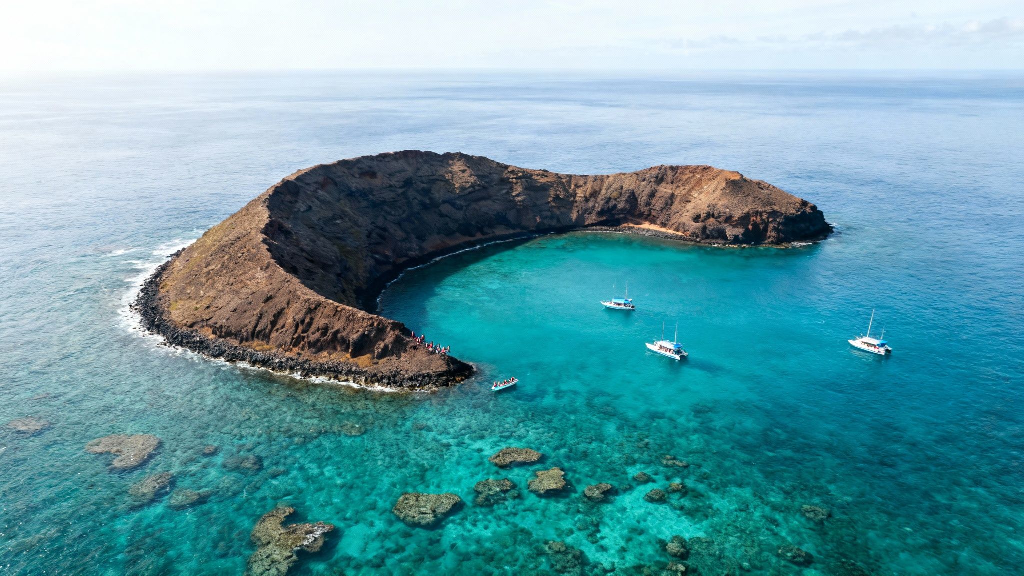 Aerial view of Molokini Crater in Hawaii, featuring boats, turquoise water, and coral reefs.