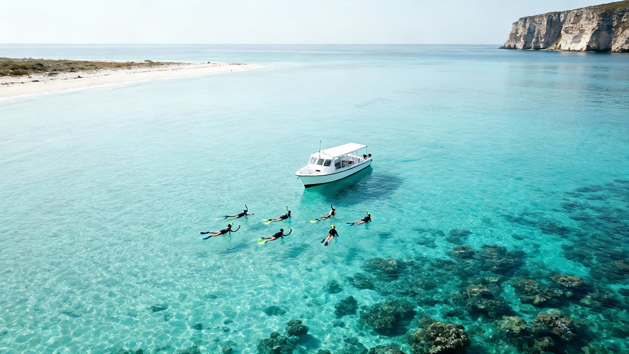 Group of snorkelers exploring crystal clear turquoise water with white boat and coastal cliffs