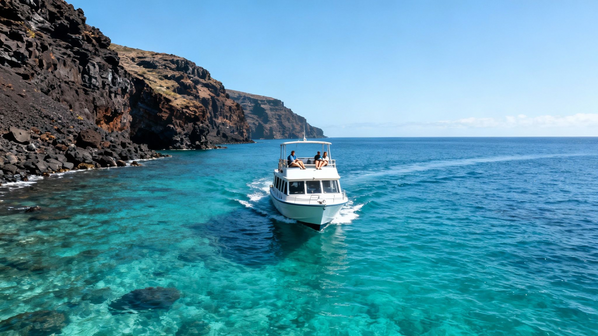 White boat carrying three people cruises clear turquoise water past dark rocky cliffs under a blue sky.