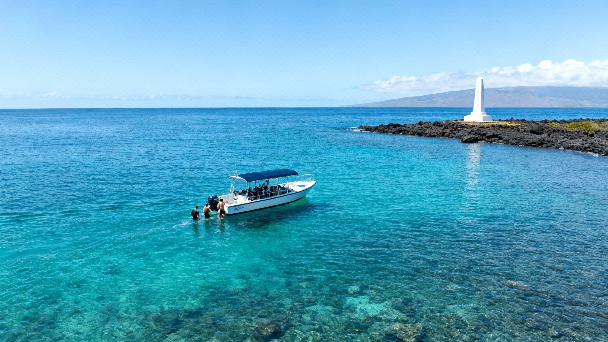 A boat with people swimming in clear turquoise water near a white monument on a volcanic shore.