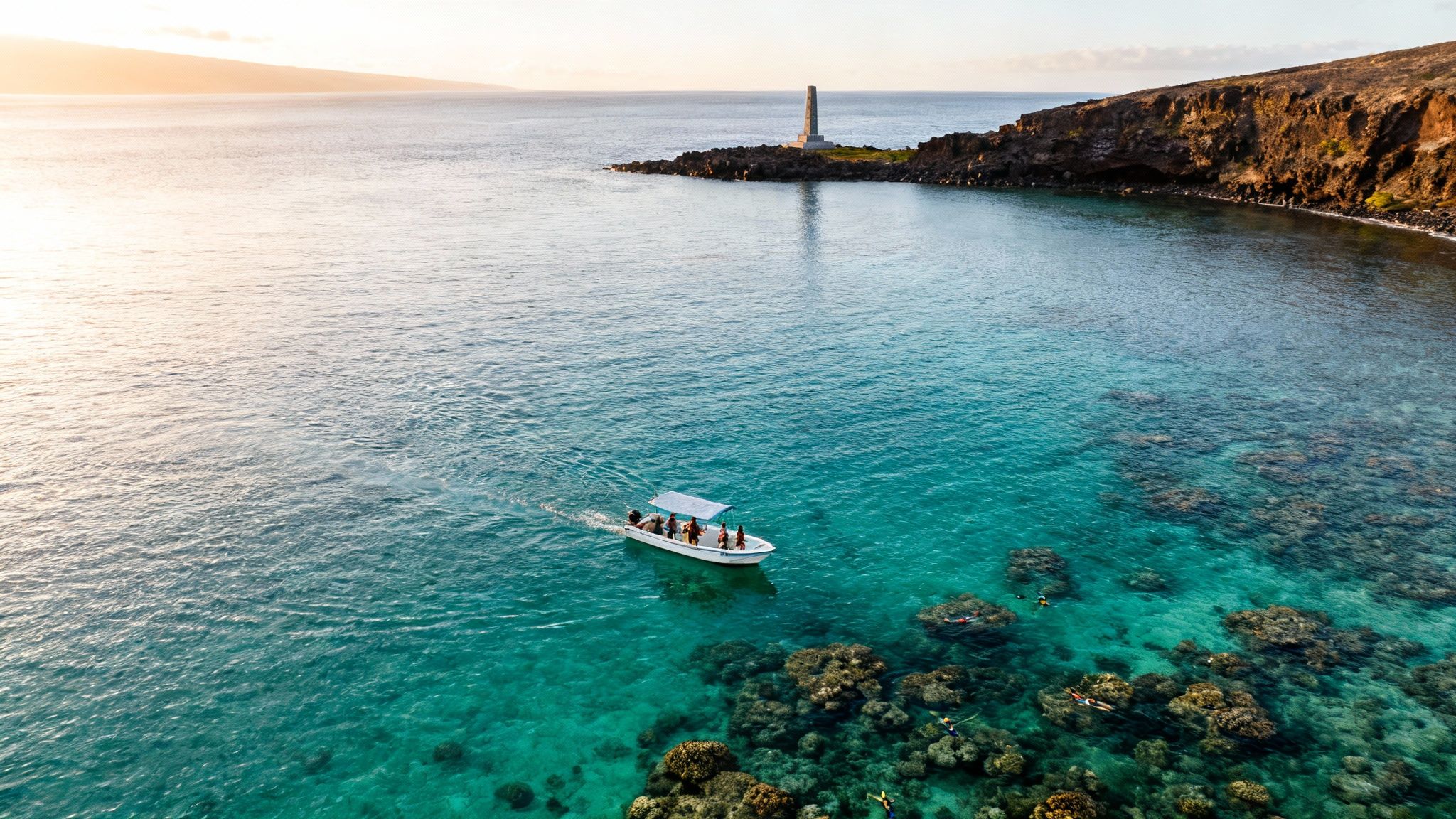 Aerial view of a boat with snorkelers in clear turquoise water near a lighthouse at sunset.