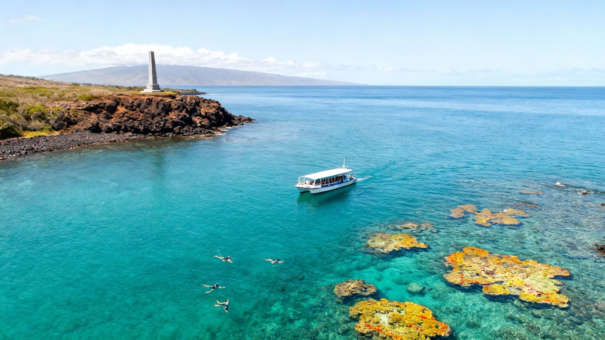 Aerial view of Kealakekua Bay, Hawaii, with a monument, snorkelers, boat, and colorful coral reef.