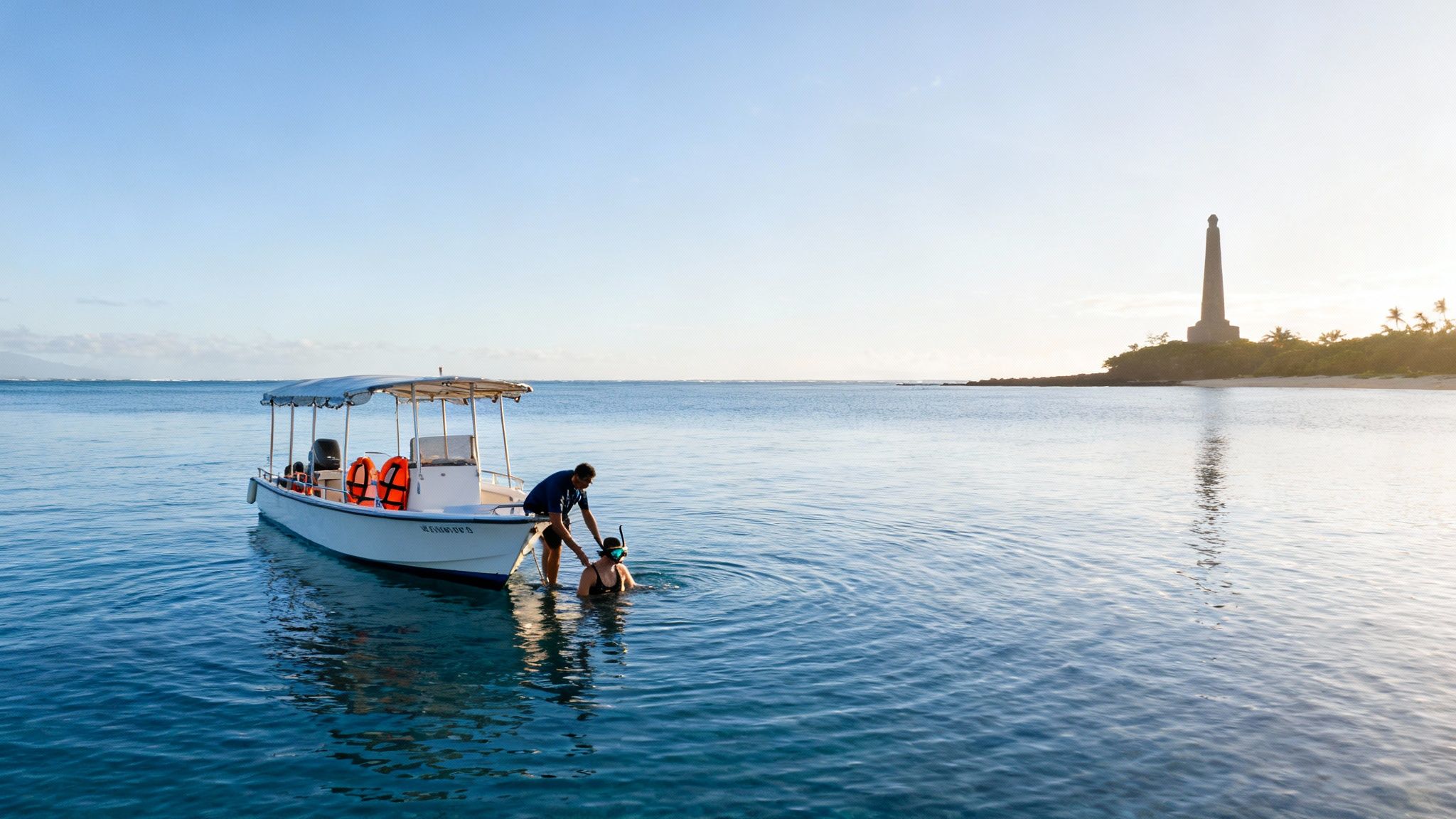 Man helps person in snorkeling gear get into clear blue ocean water near a boat and a monument.