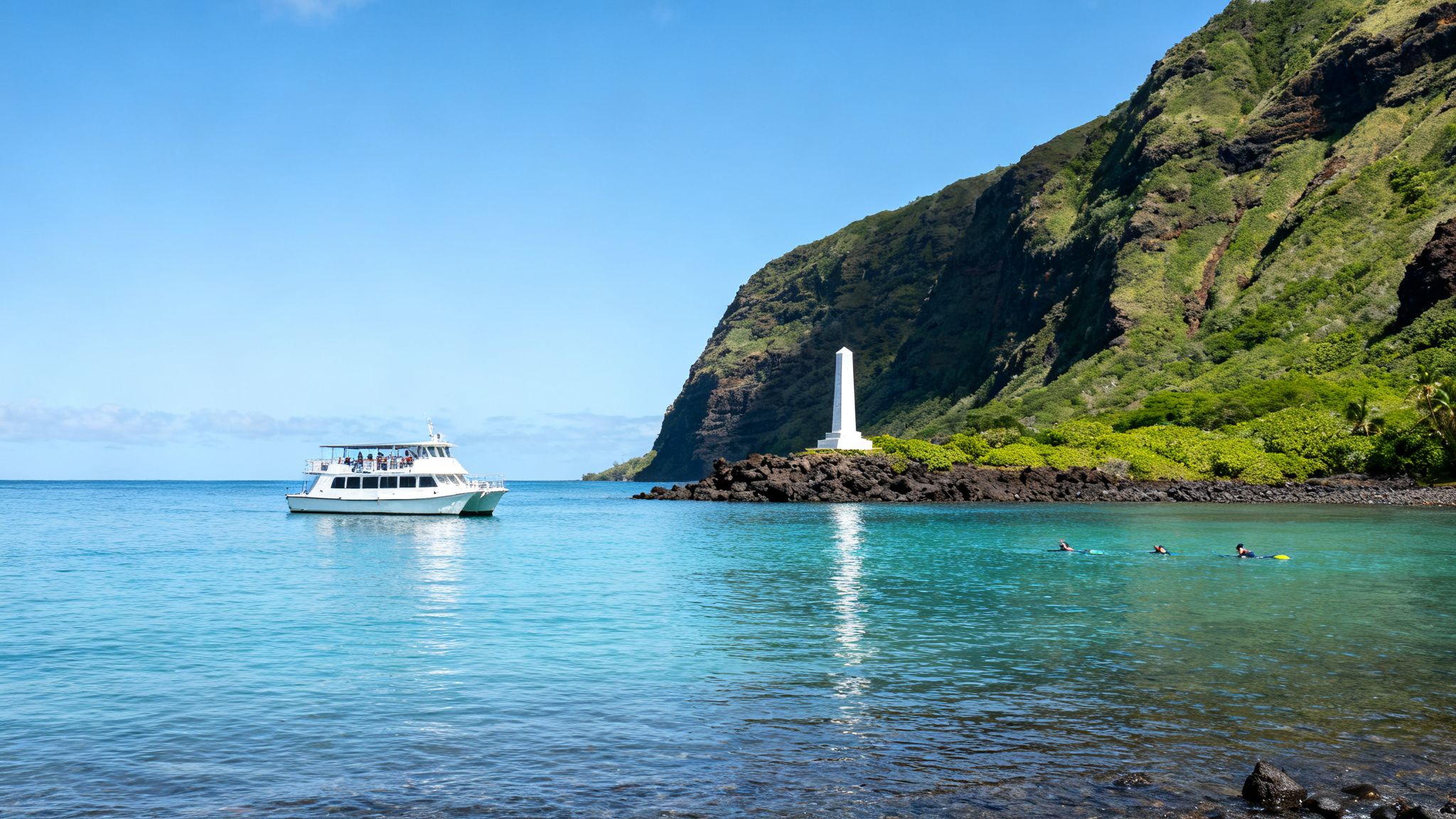 A tour boat and snorkelers in clear turquoise water near a white monument and green mountains.