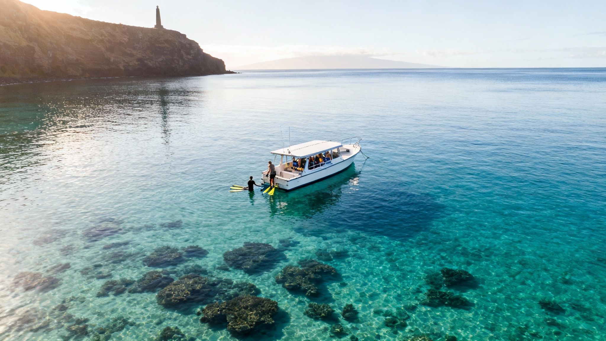 Aerial view of a boat with people snorkeling in clear turquoise water near a rocky coast.