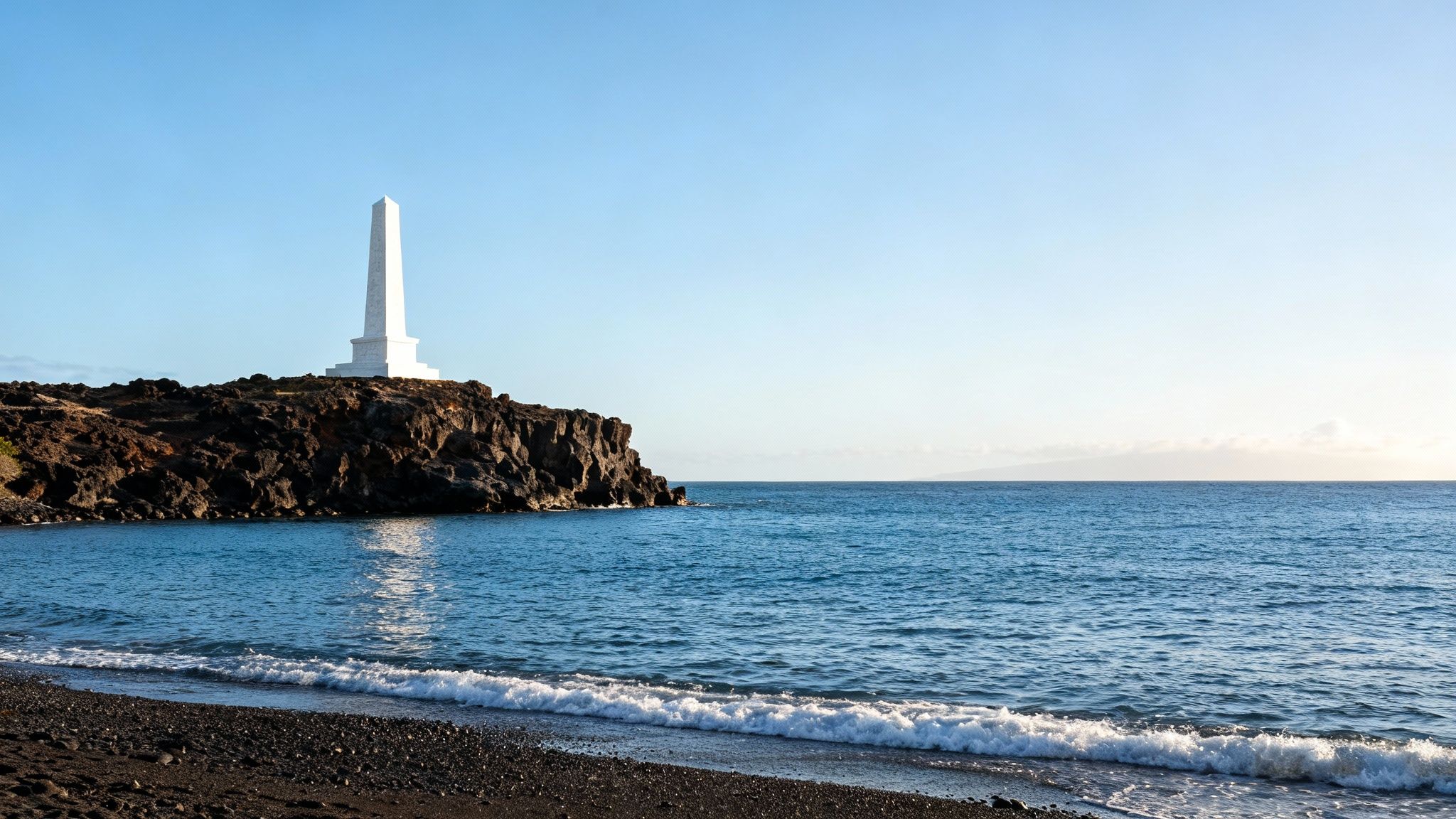 Historic white obelisk stands tall on a rugged volcanic coastline, with ocean and black pebble beach.