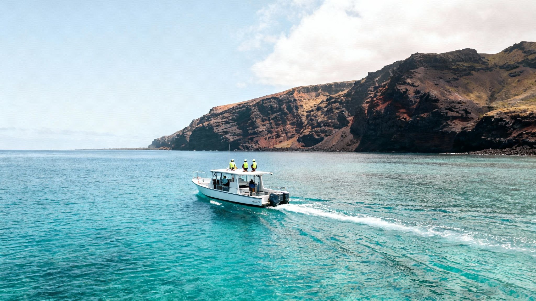 A white boat with passengers in life jackets cruises on bright turquoise water near towering volcanic cliffs.