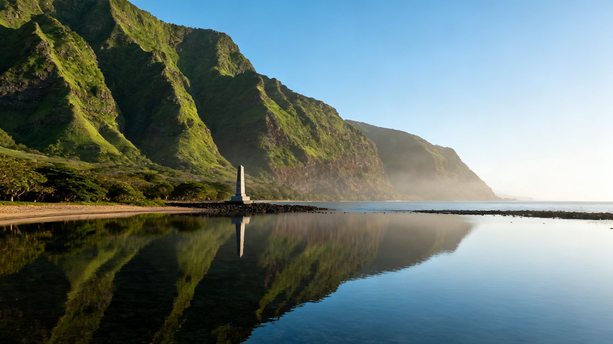 Verdant mountains reflecting in serene coastal waters with a historical monument at sunrise.