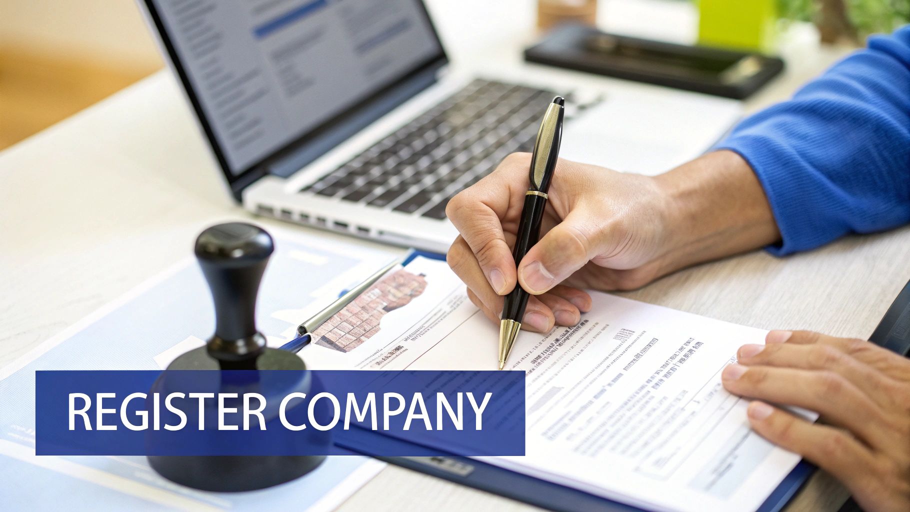 A person's hands signing a document on a desk with a laptop and a company stamp.