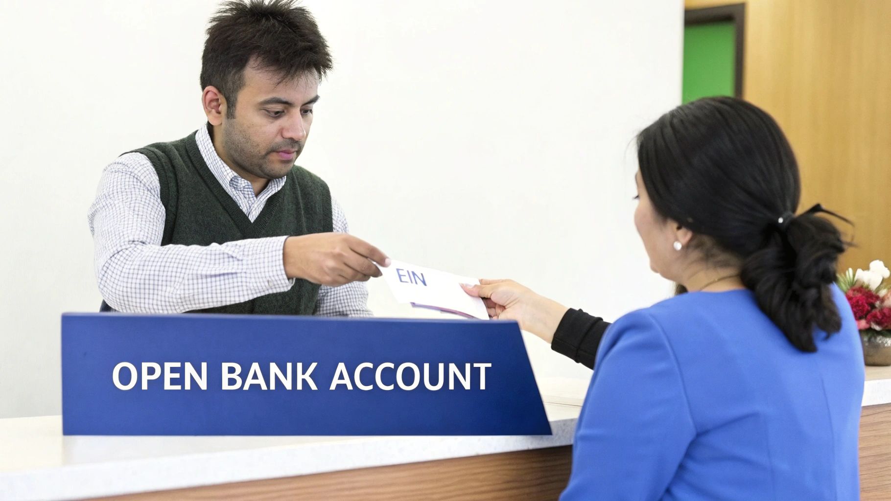 A man hands an EIN document to a woman at a counter with an "OPEN BANK ACCOUNT" sign.