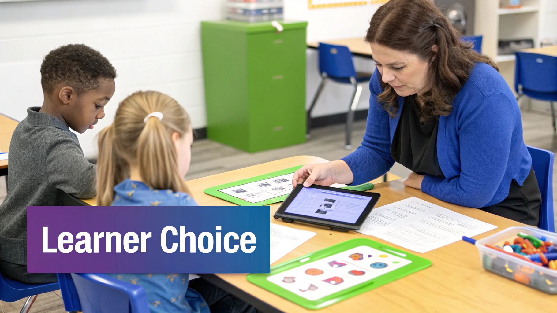 Teacher helps two young students with a tablet in a modern, collaborative classroom environment.