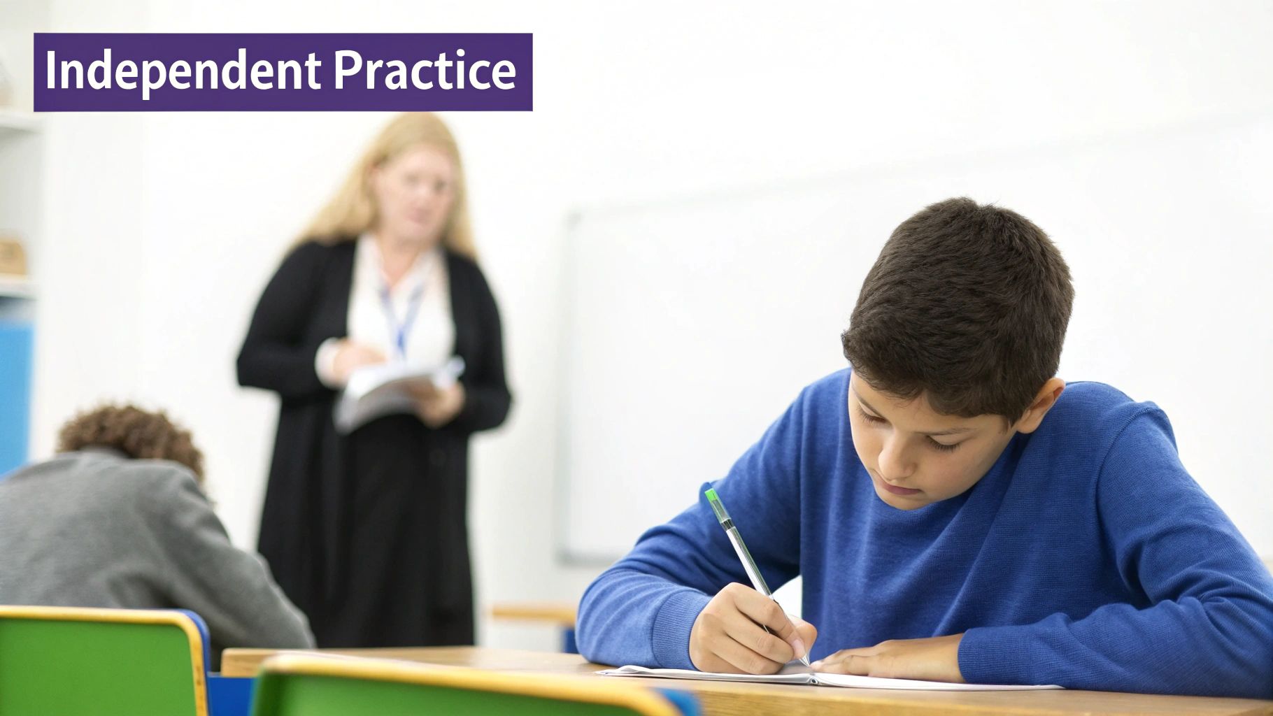 A student in a blue sweater writes at a desk, demonstrating independent practice in class.