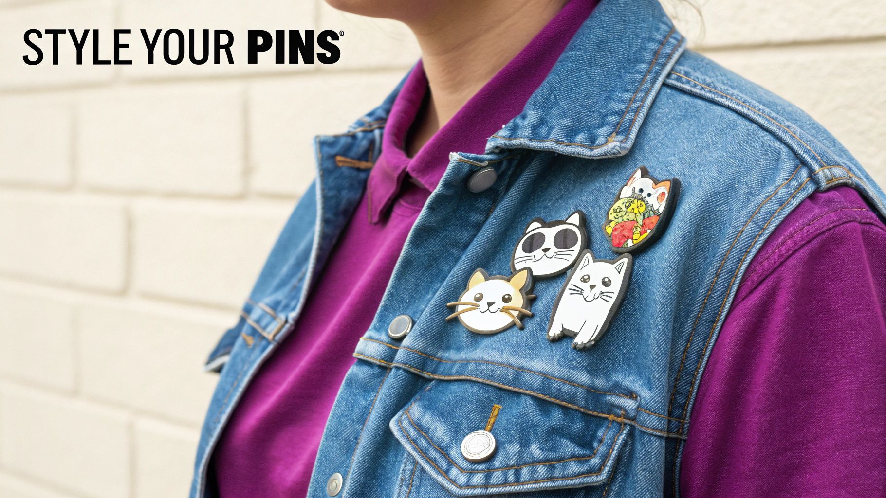 A denim jacket featuring several playful cat enamel pins, worn over a purple shirt.