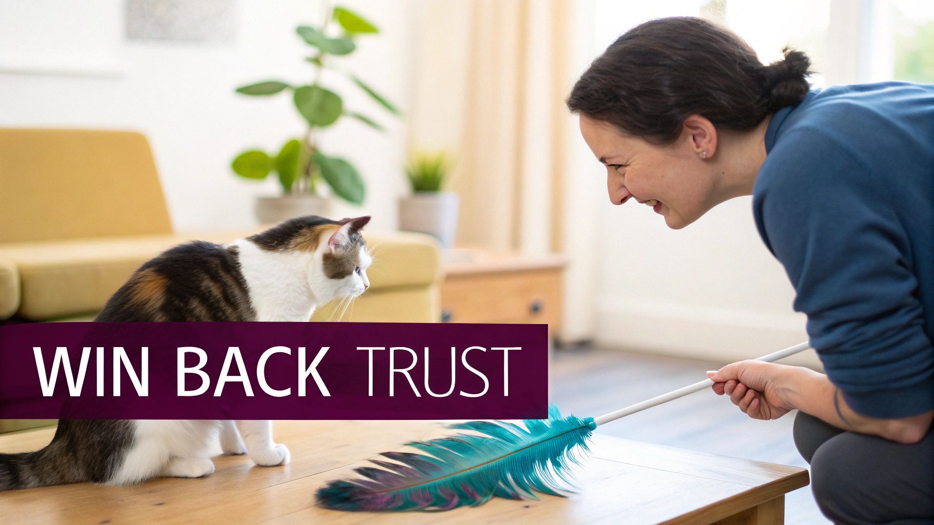 A woman happily playing with a calico cat using a feather wand toy on a wooden table.