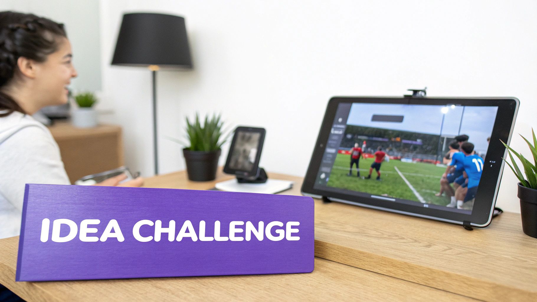 Smiling person watches a sports game on a tablet, with an "IDEA CHALLENGE" sign nearby.