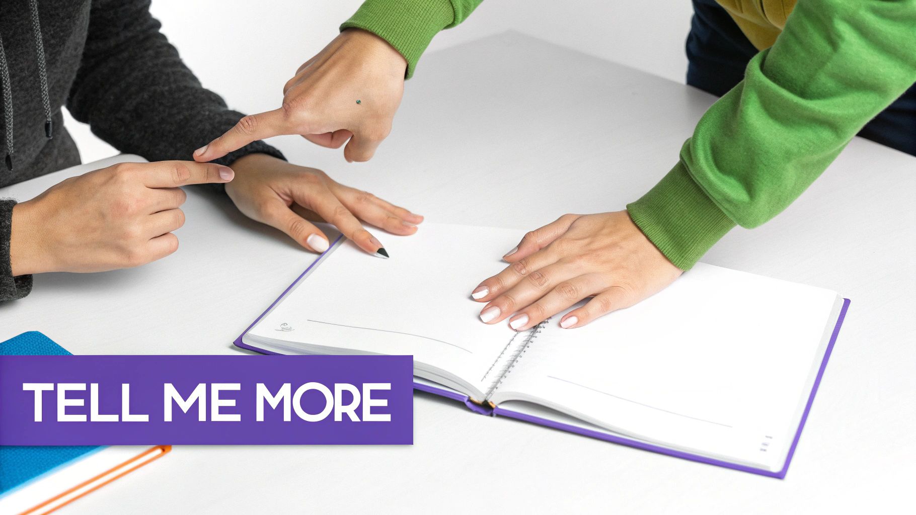 Two people interact over an open notebook on a white desk, one pointing at the other's hand, with 'Tell Me More' text.