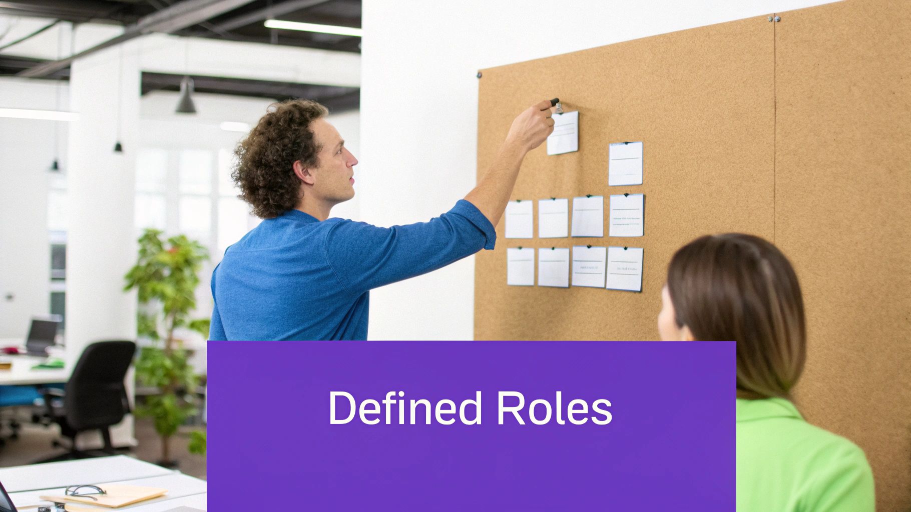 A man places a note on a cork board during a team meeting, illustrating defined roles.