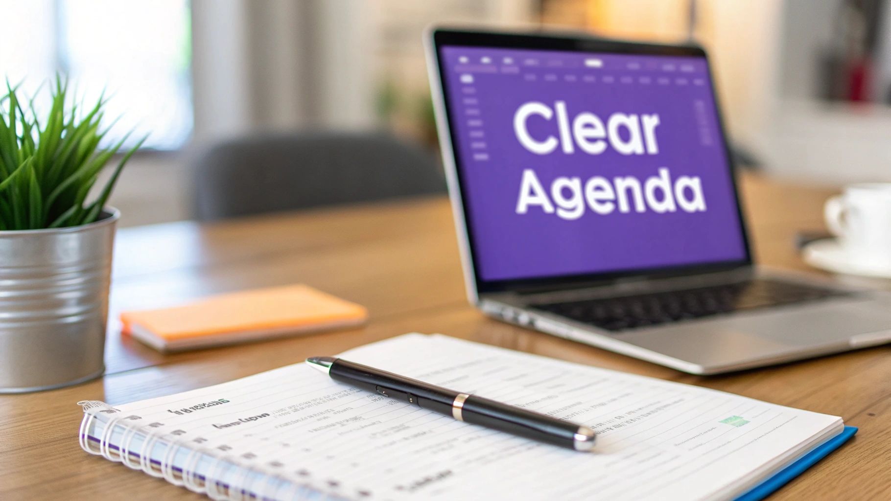 A meeting setup with a laptop showing "Clear Agenda," a notebook, pen, and plant on a wooden desk.