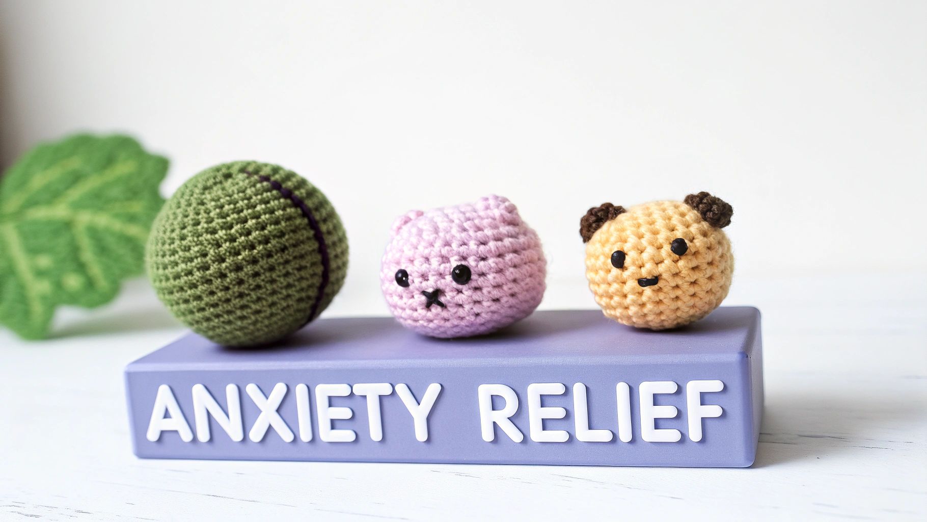 A collection of small, colorful crocheted fidget objects, including a textured ball, a squishy creature, and a worry stone, held in someone's hands.