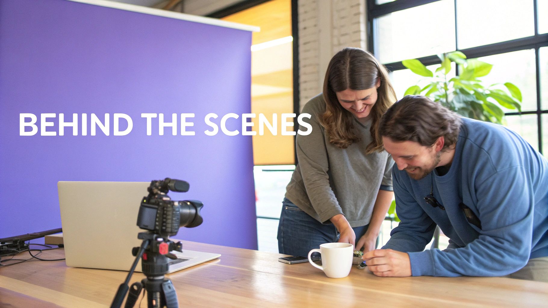 Behind-the-scenes shot of two smiling people collaborating on video content creation with a camera.