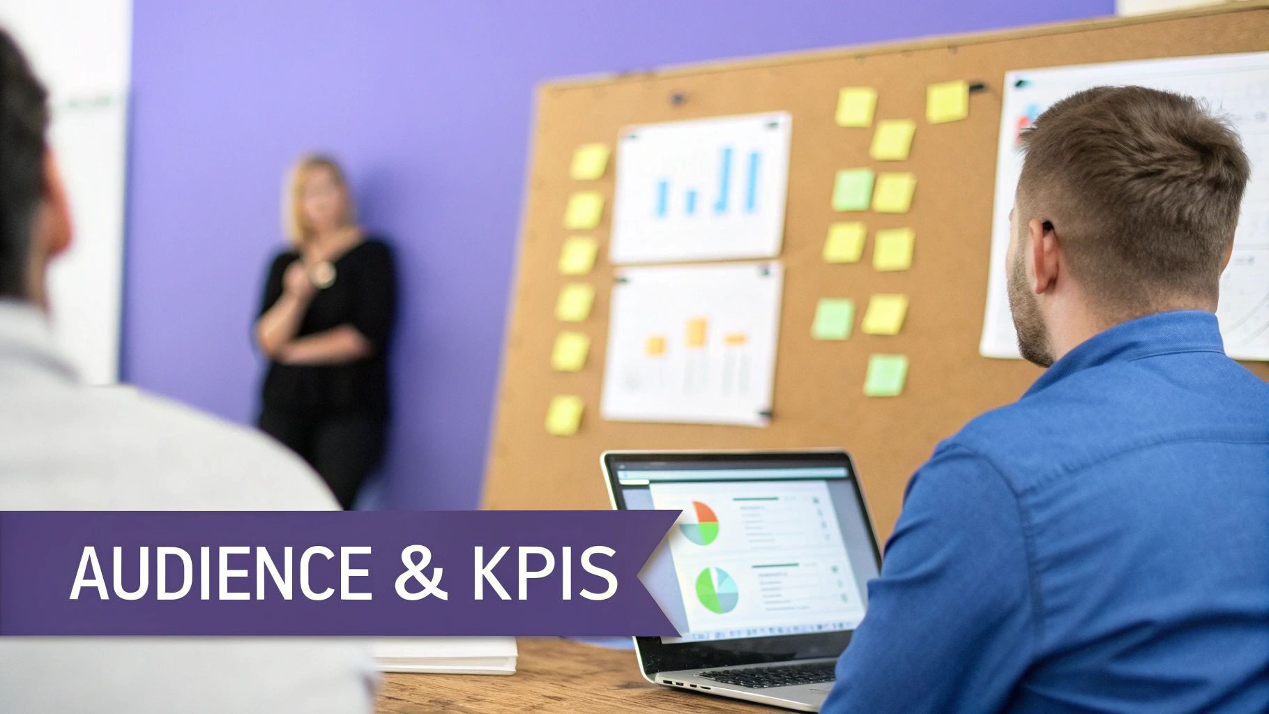 A person views a laptop displaying charts and a corkboard with data during a work meeting.