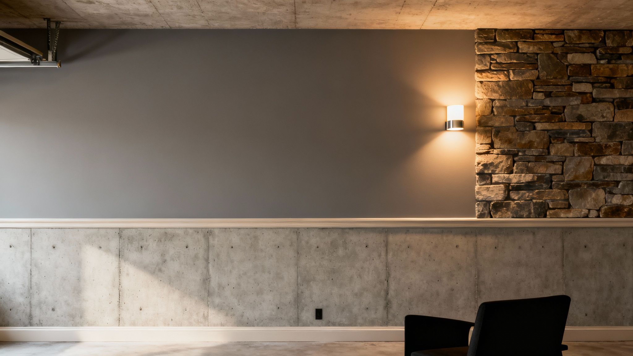 Modern basement room with grey walls, concrete wainscoting, a stone accent wall, and a sconce light.