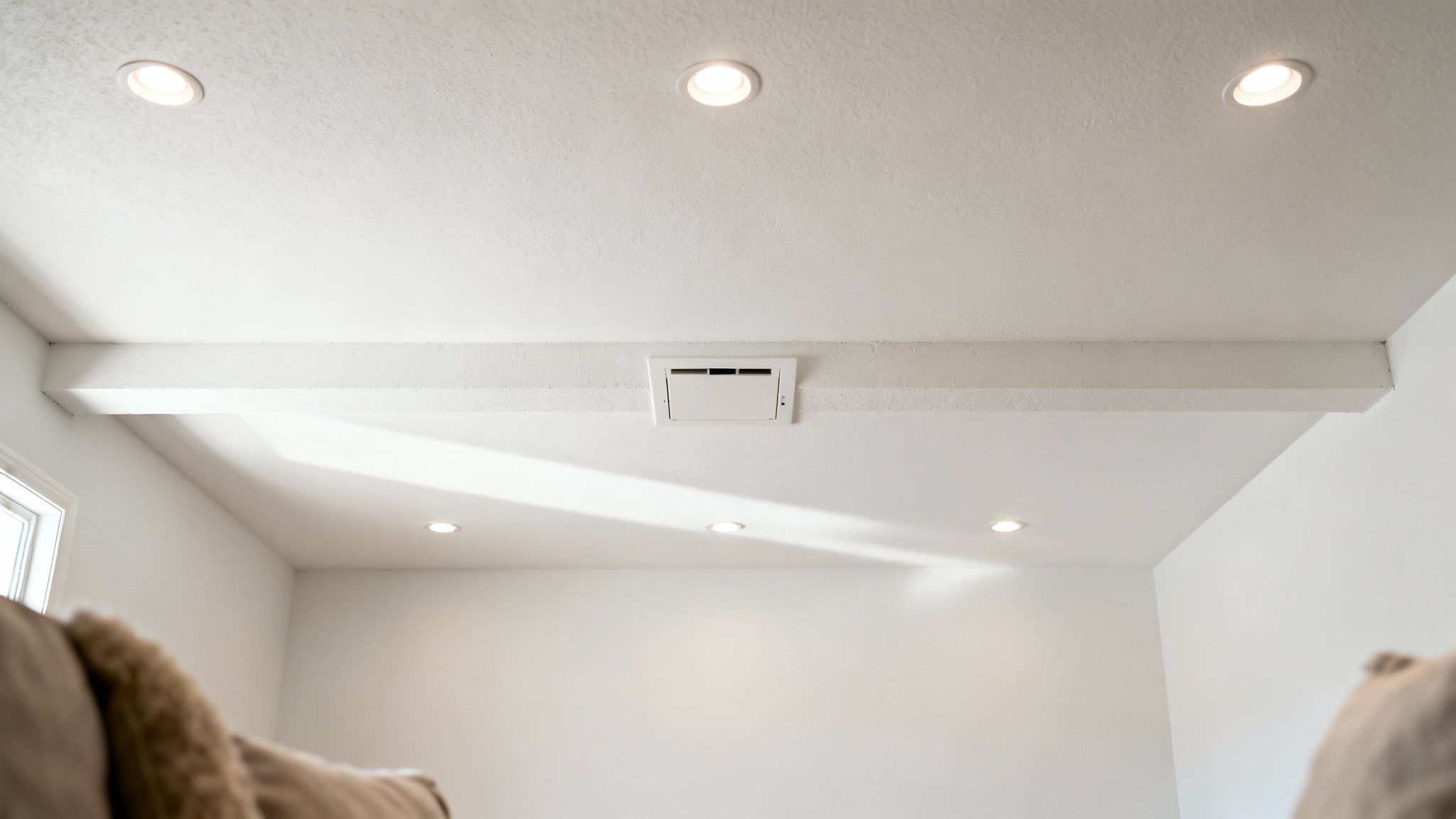 A clean white basement ceiling with recessed lighting, an HVAC vent, and decorative beams.
