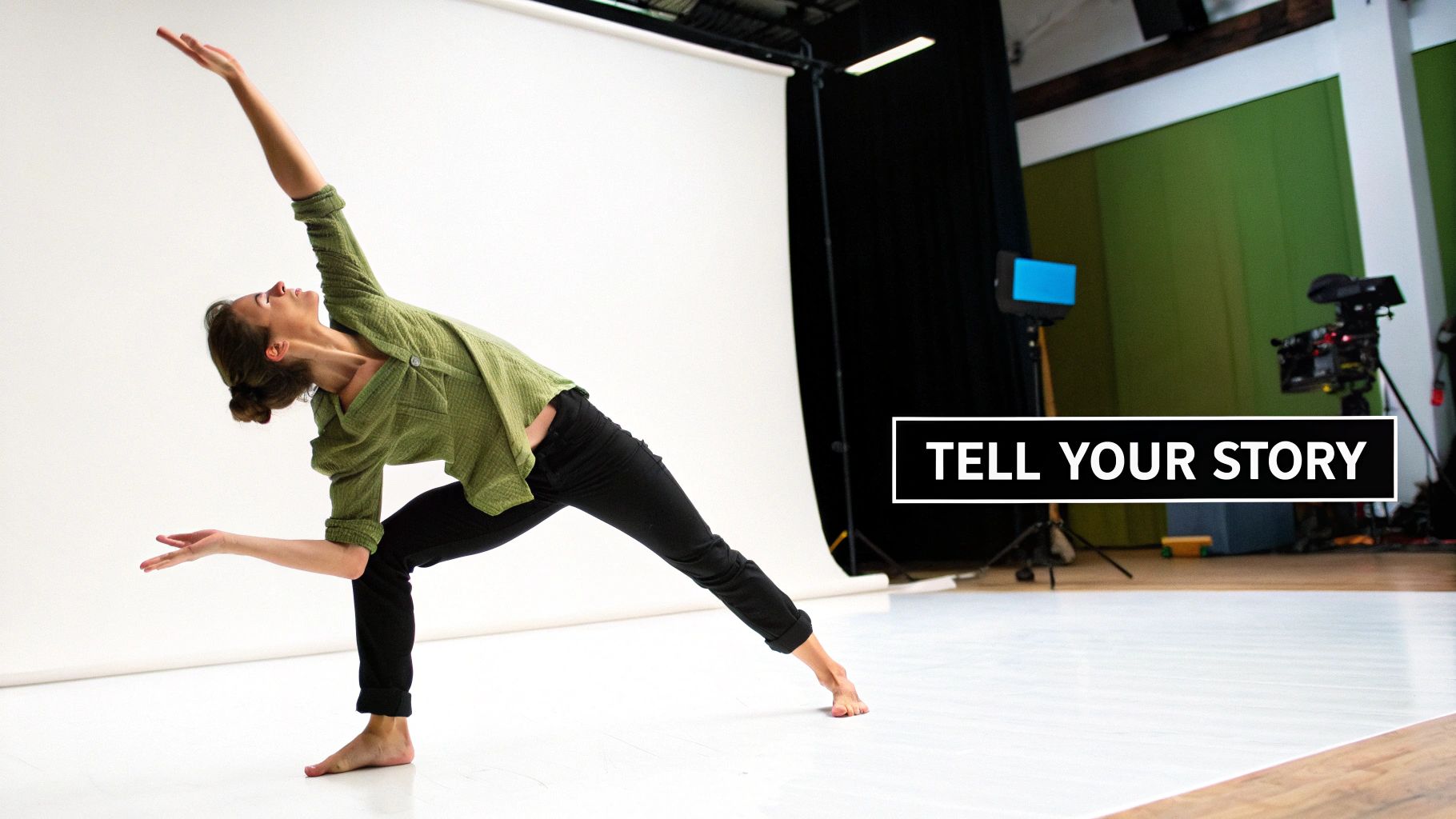 A barefoot woman in a green top dances in a studio, extending her arms elegantly against a white backdrop.