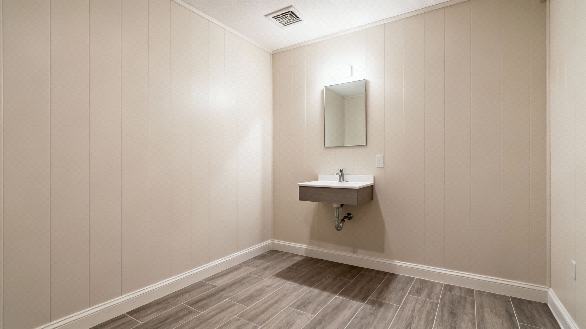 A clean, newly installed basement bathroom featuring a floating vanity, mirror, and tiled floor.