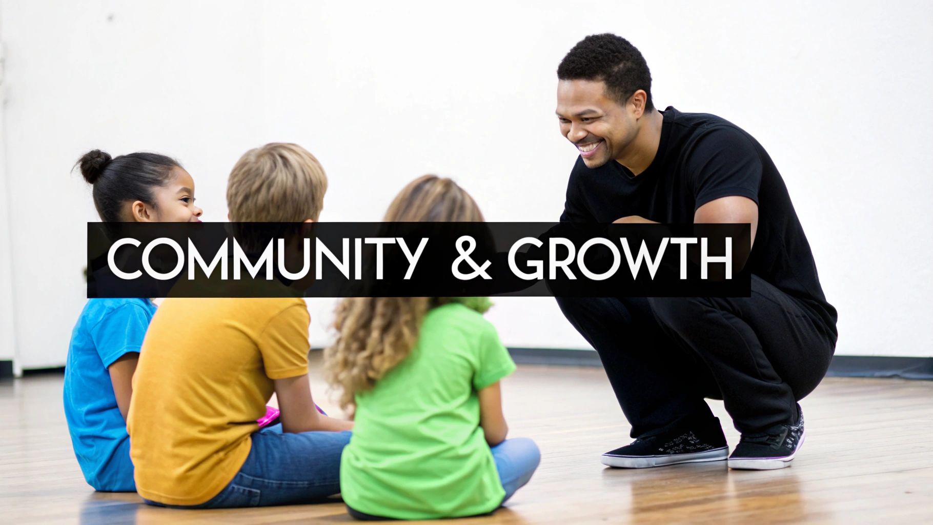 An adult male smiles while interacting with three children sitting on a wooden floor.
