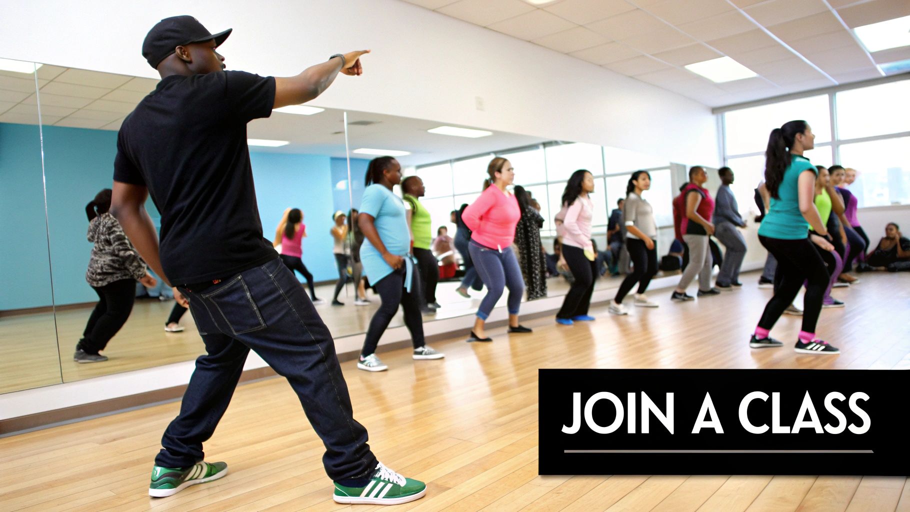 A male instructor leads a lively dance class with diverse students mirroring his moves in a bright studio.