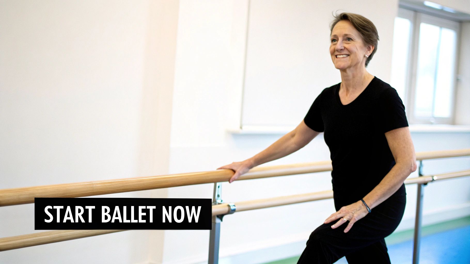 A smiling senior woman in black activewear holding a wooden ballet barre in a dance studio.