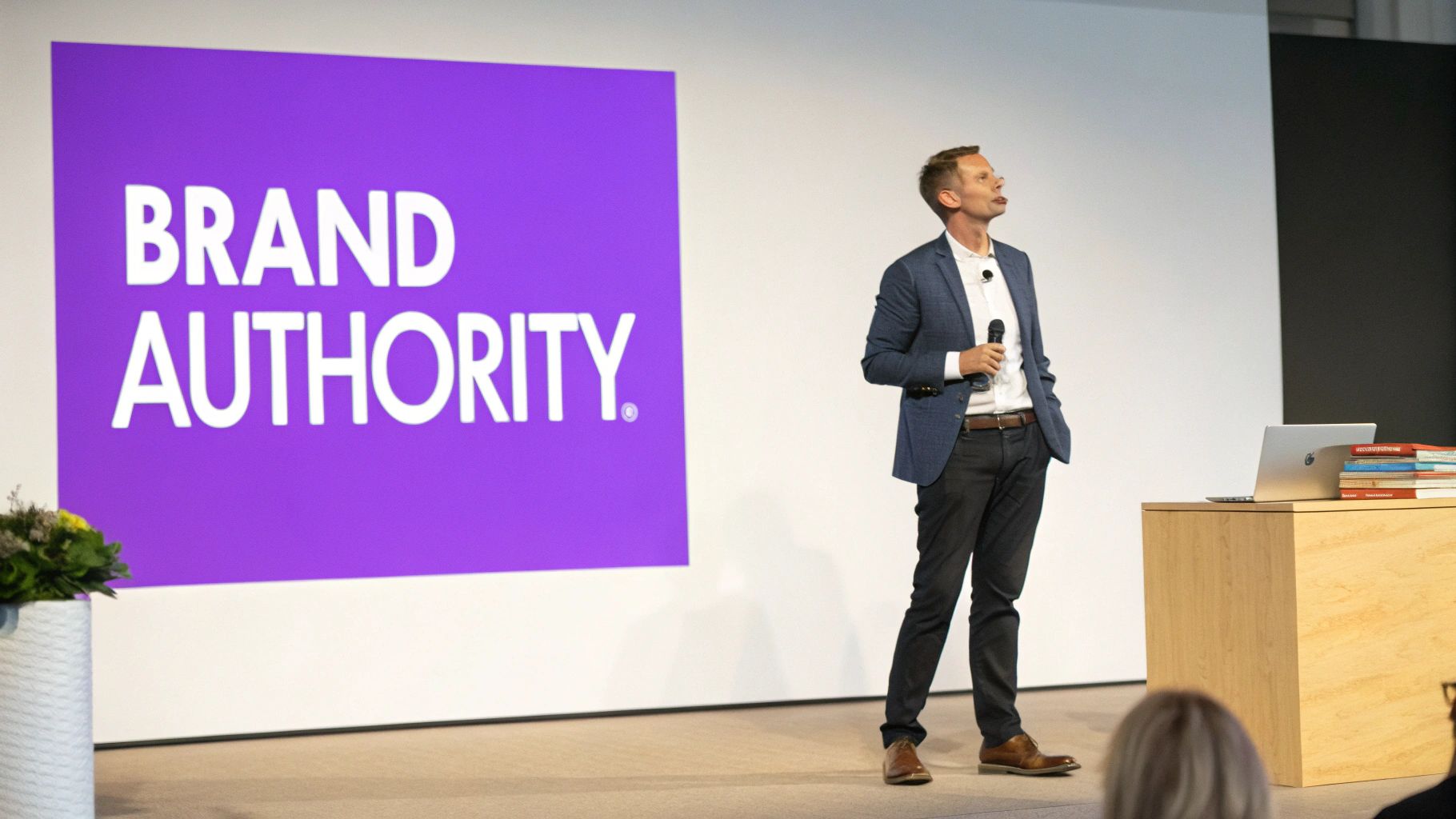 A man in a suit gives a presentation on stage with "BRAND AUTHORITY" displayed on a large screen.