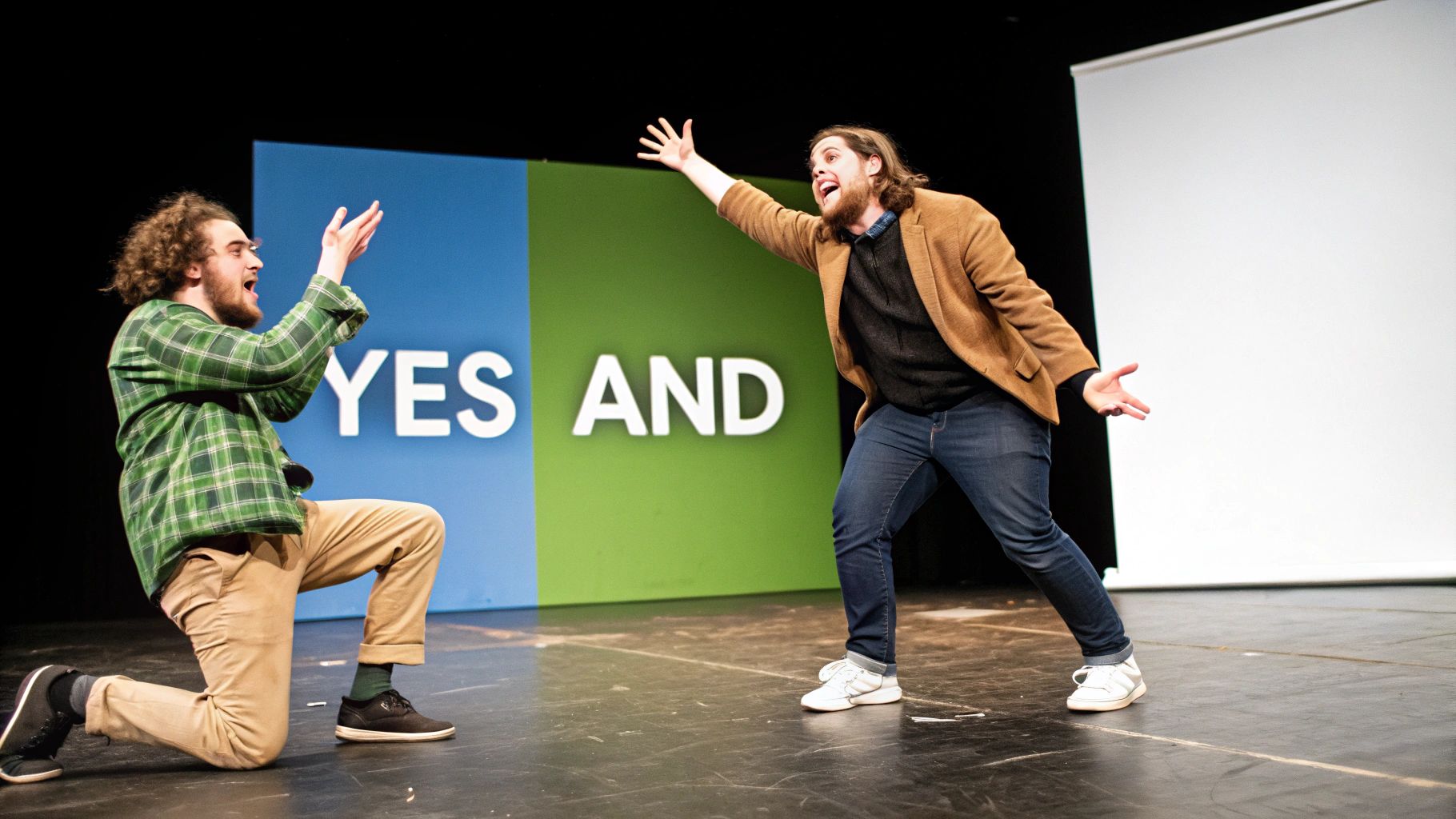 Two enthusiastic men performing an improv scene on stage, one kneeling and the other standing, with a "YES AND" backdrop.