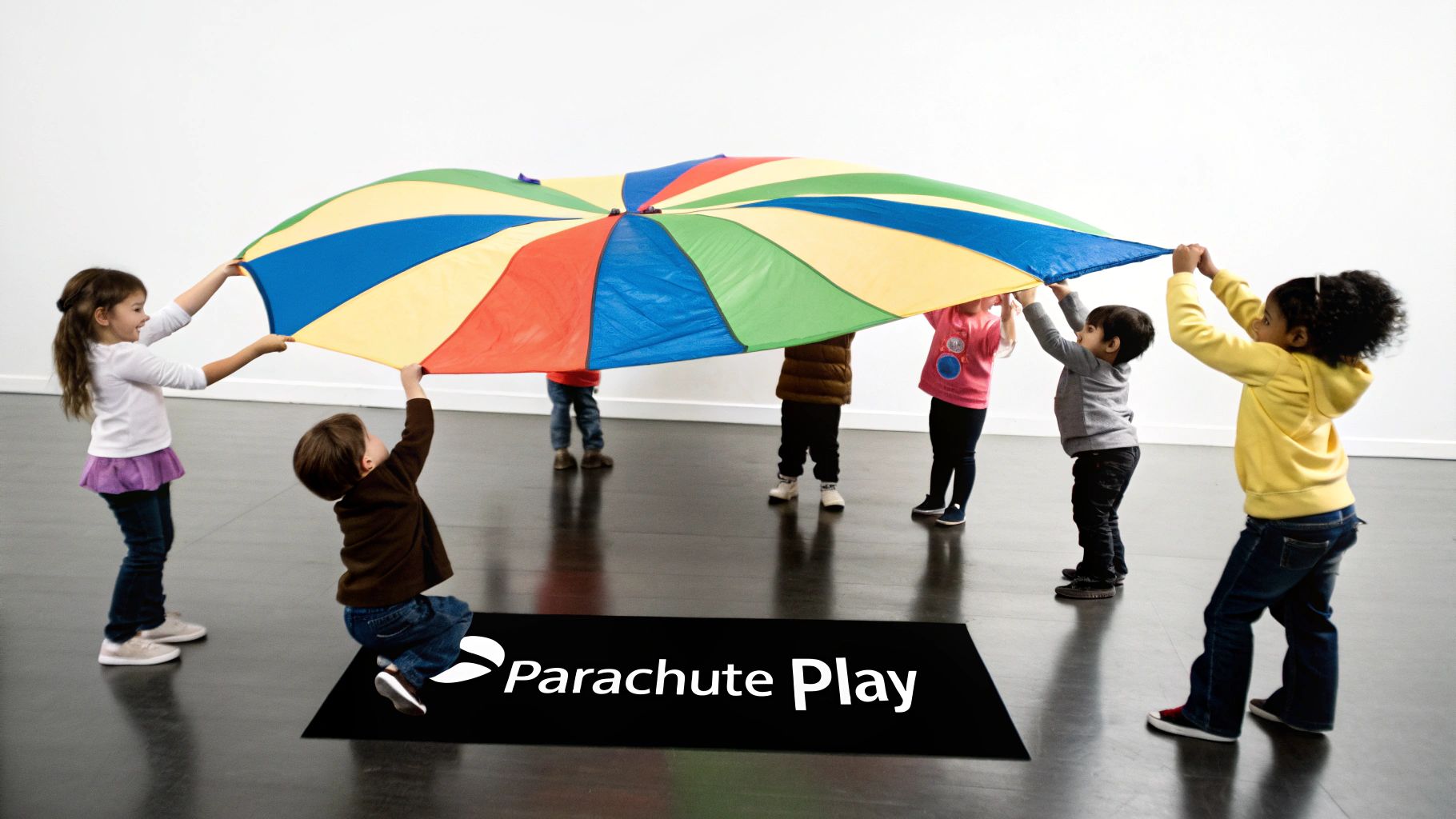 Preschoolers joyfully lifting a vibrant rainbow parachute during an indoor group play activity.