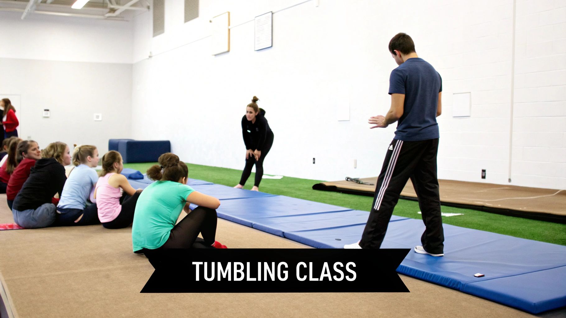 A group of young women watching instructors demonstrate skills during a tumbling class in a gym.