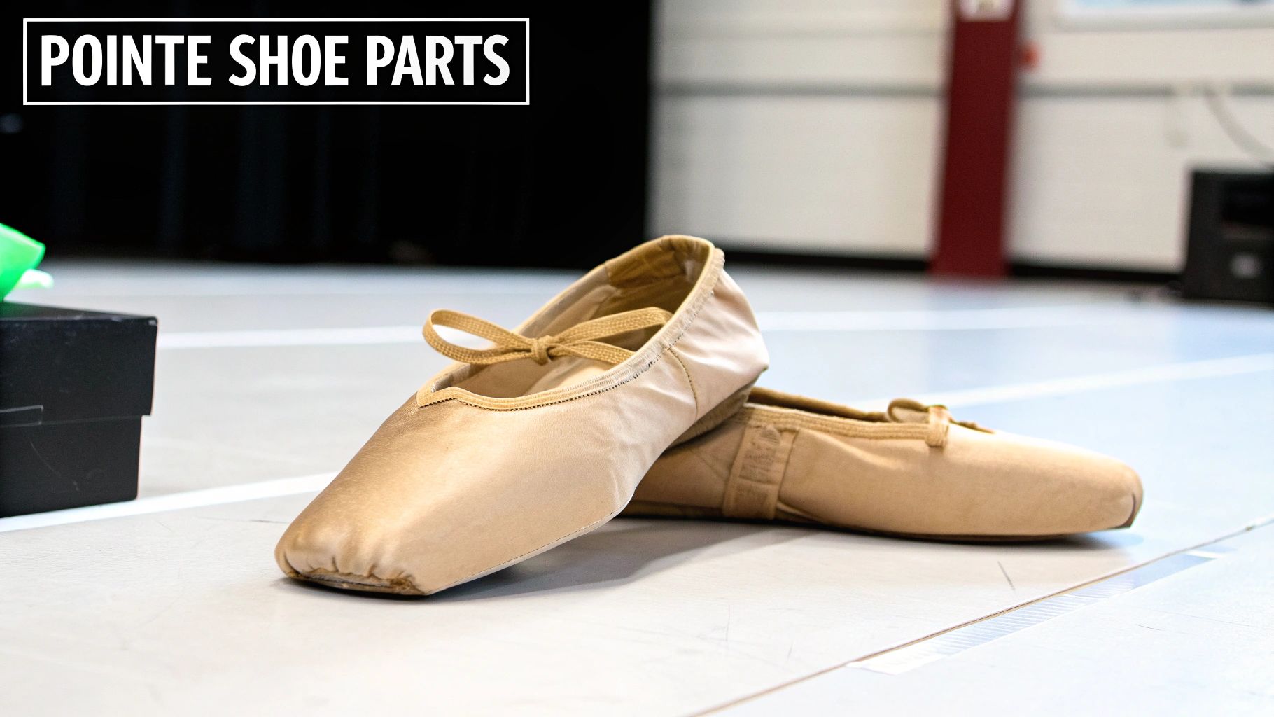Two beige satin pointe ballet shoes with ribbons lie on a light studio floor.