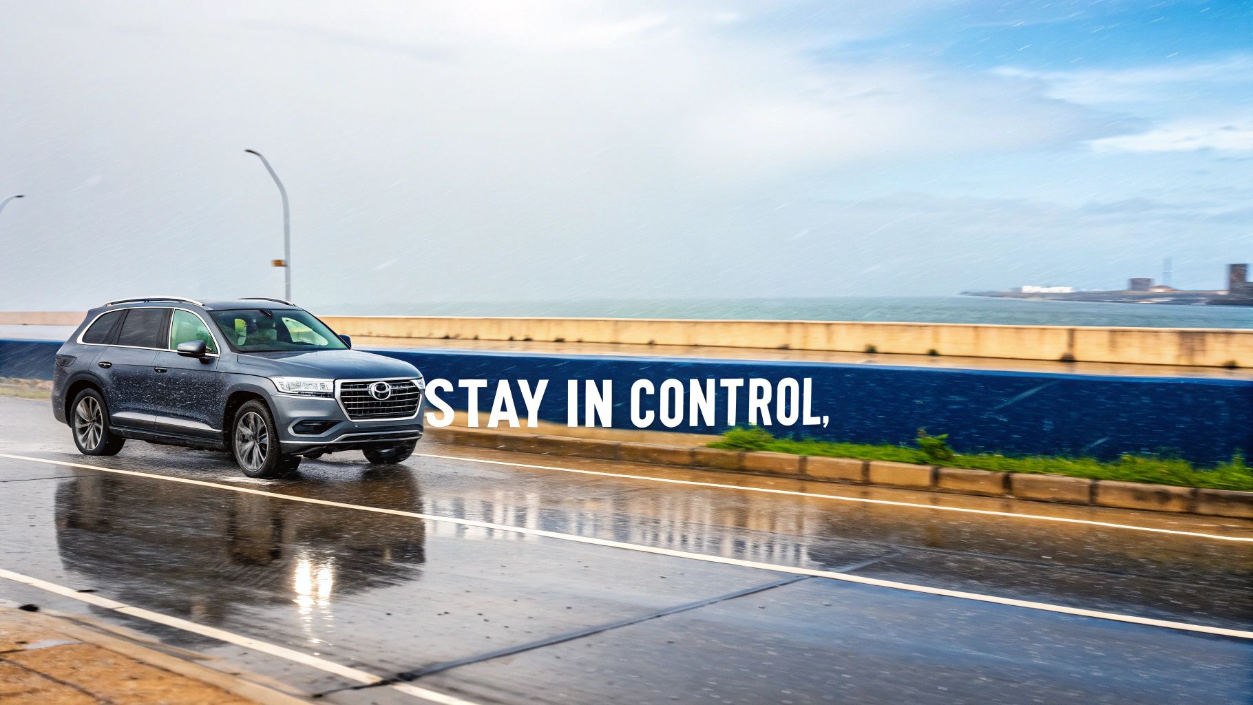 A grey SUV drives on a wet, rainy road next to the ocean on a cloudy day.