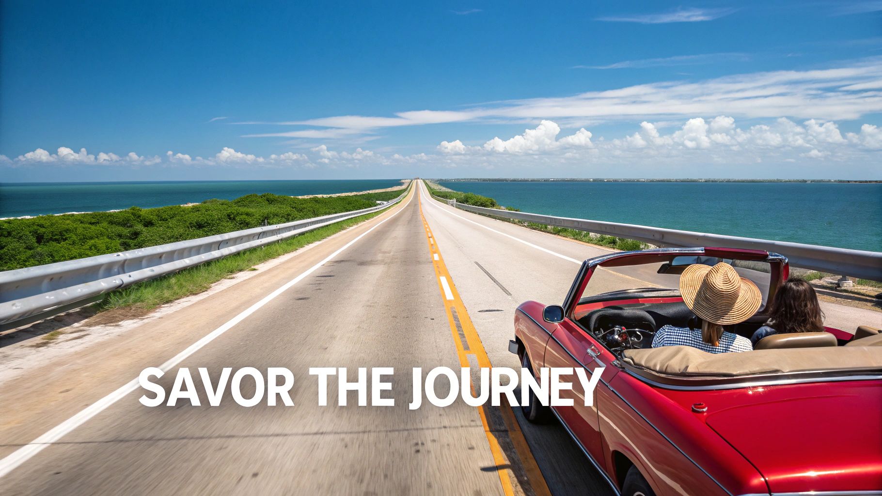 Two people in a red convertible driving on a scenic coastal highway overlooking the ocean.