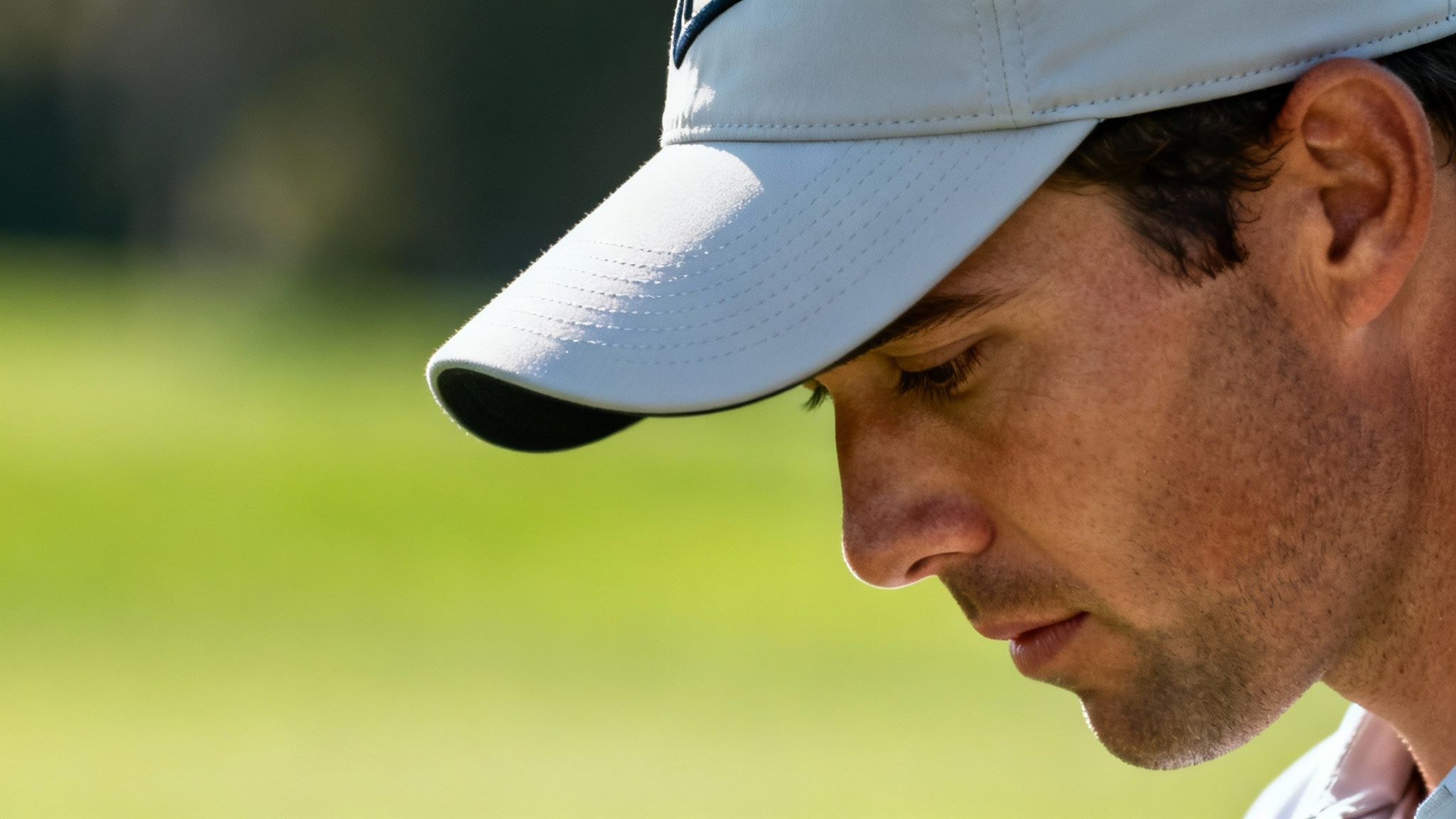 Golfer in a white hat standing on a sunny golf course, preparing to swing.