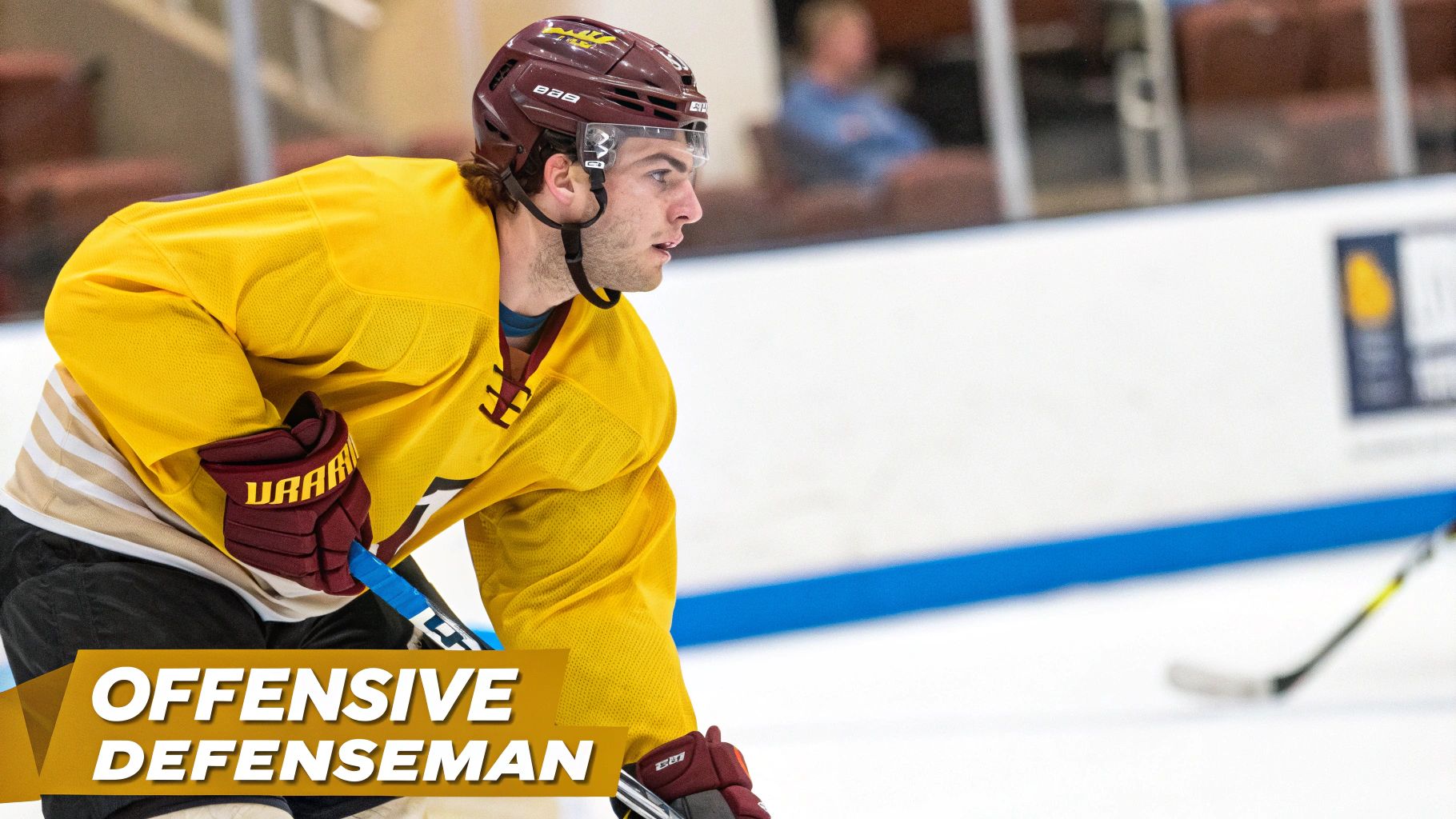 Hockey player in yellow jersey and maroon helmet skating during practice session on ice rink