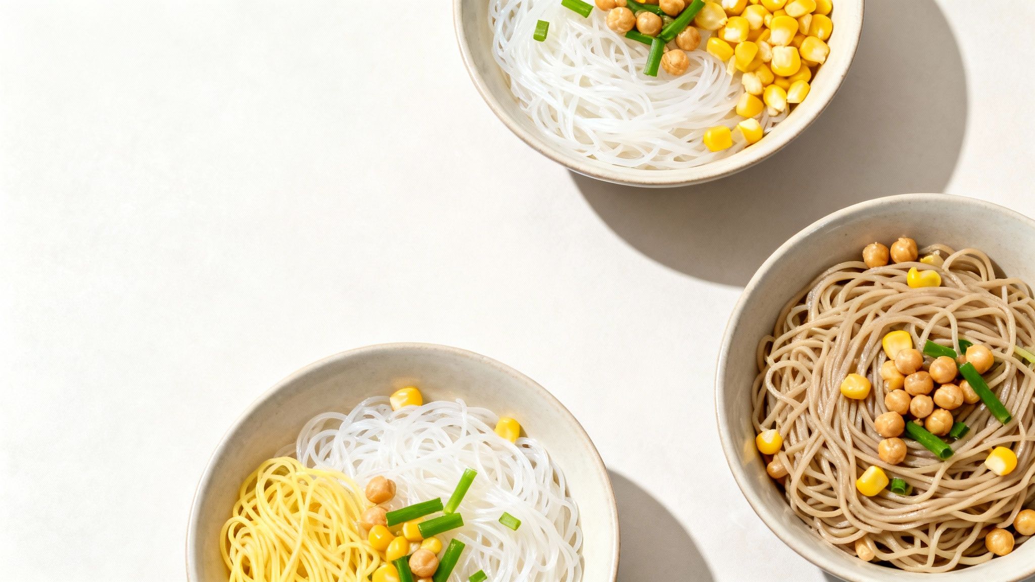 Tres cuencos de fideos con maíz, garbanzos y cebolletas verdes sobre fondo blanco.
