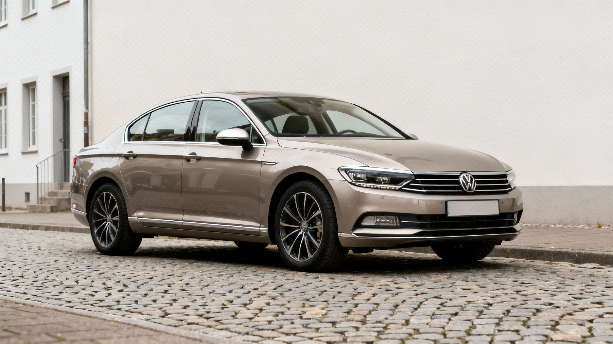 Un coche Volkswagen Passat dorado aparcado en una calle adoquinada con un edificio blanco al fondo.