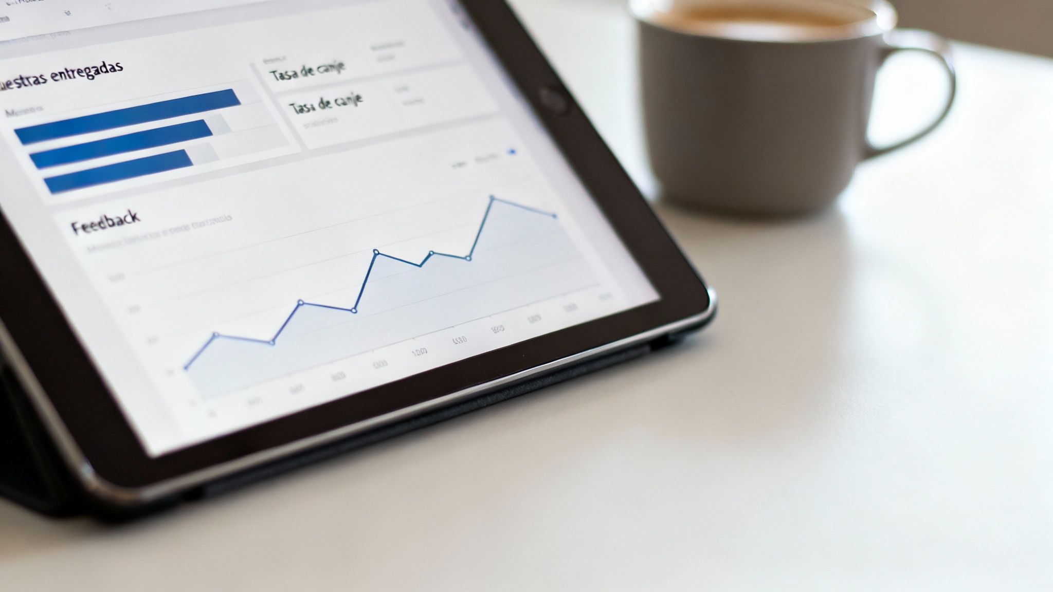 Tablet con gráficos de análisis de datos de negocio y una taza de café sobre una mesa blanca.