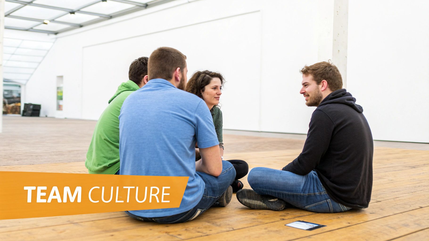 Four diverse people sitting on a wooden floor in a circle, engaged in a team discussion, with "TEAM CULTURE" text overlay.