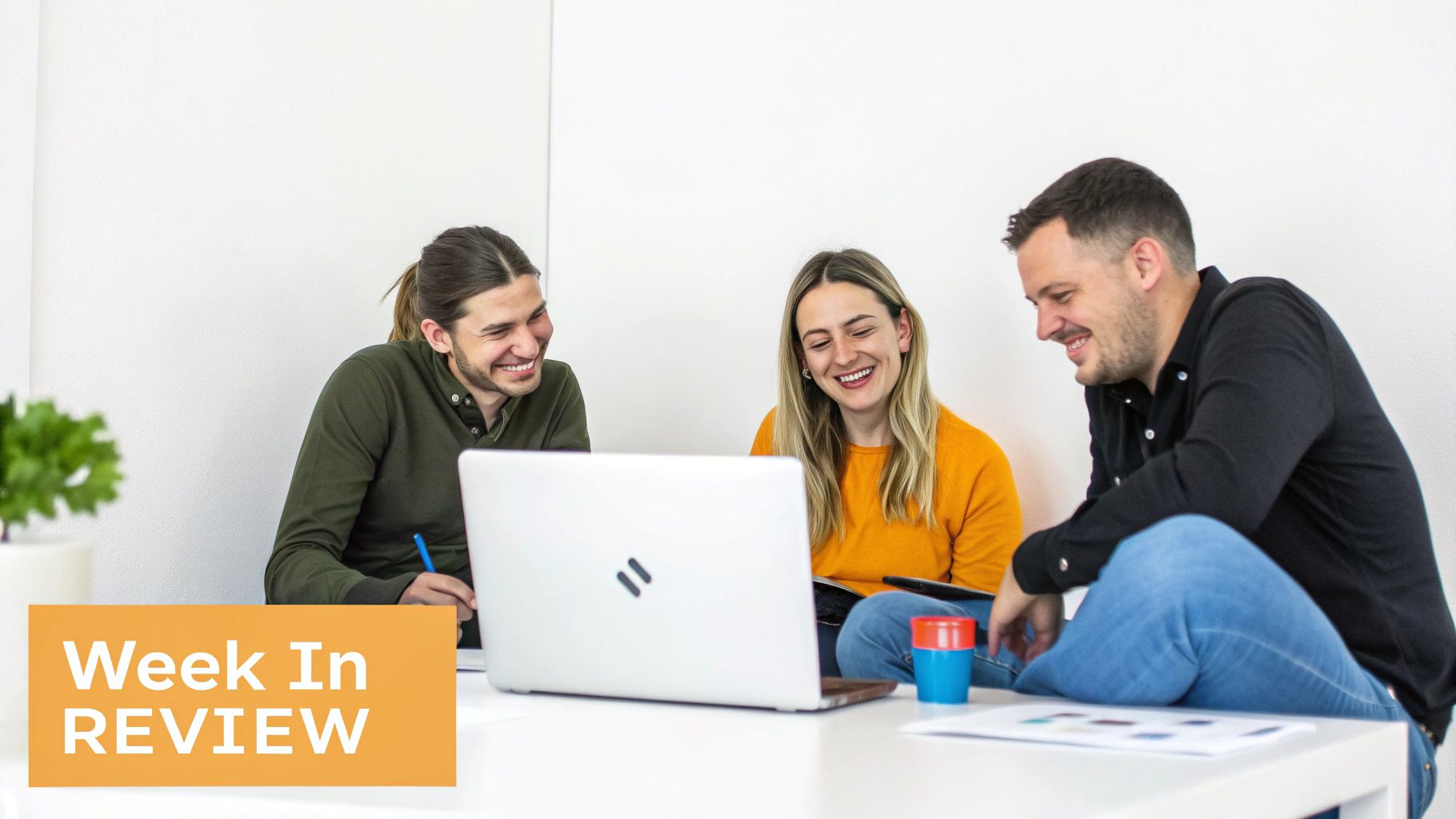 Three happy colleagues smiling and laughing while collaborating around a laptop during a meeting.